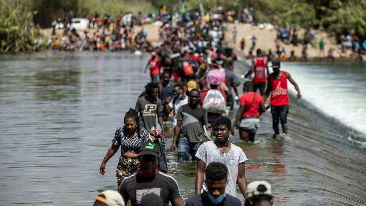A line of migrants, mostly Black, cross a river