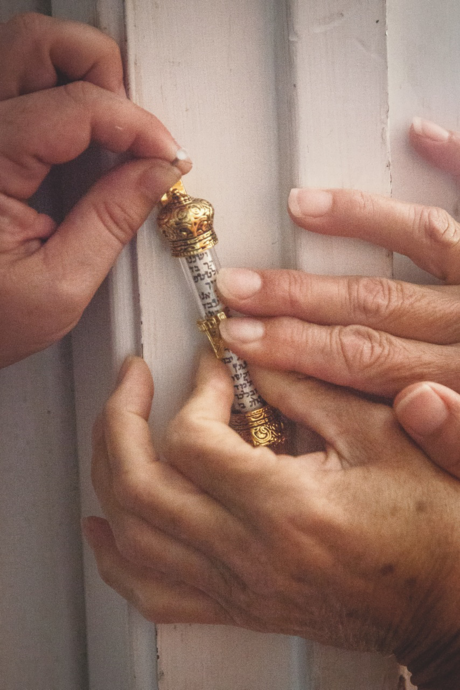 A closeup of two sets of hands hold up a mezuzah set to be fixed to a doorpost