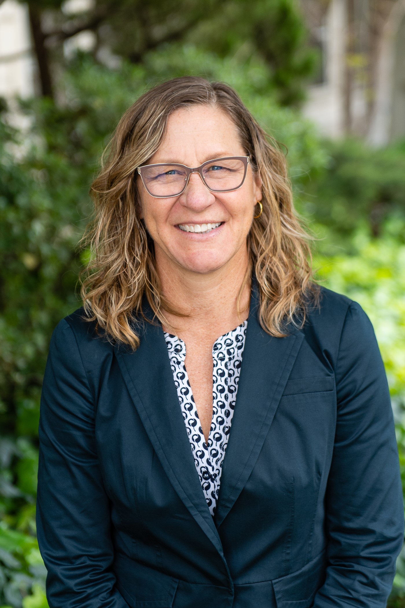 Hillary Hoyne's headshot. She is a white woman with a big, joyful smile. She has wavy shoulder length blonde hair and wears a navy blue jacket.