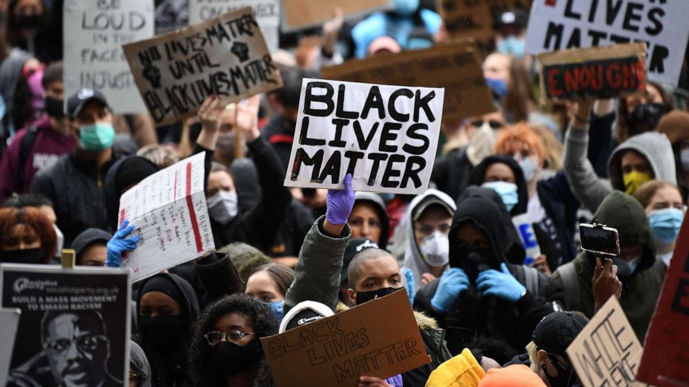 A racial justice protests; one placard featured prominently reads 'Black Lives Matter' in bold black ink'