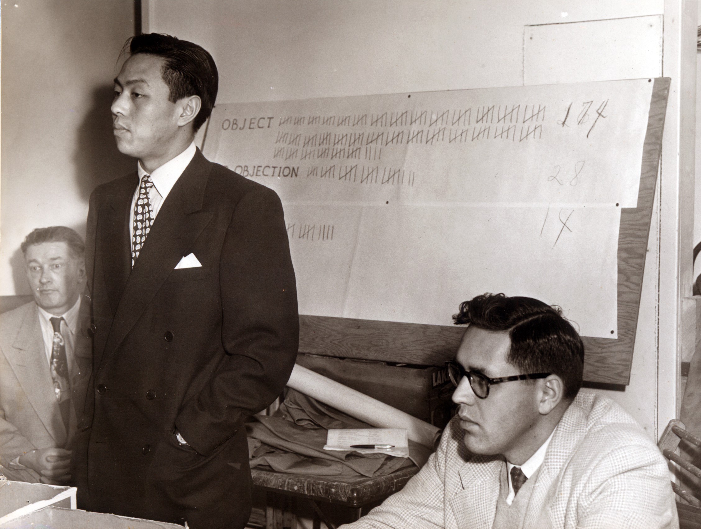 photo: Sing Sheng (left) addresses the crowd of Southwood residents after City Manager Emmons McClung (right) records the results of the vote. The board displays the final tally; 174 out of 202 residents objected to the Sheng family moving into Southwood. Courtesy of San Mateo County Historical Association Collection (SMCHA 2017.54).