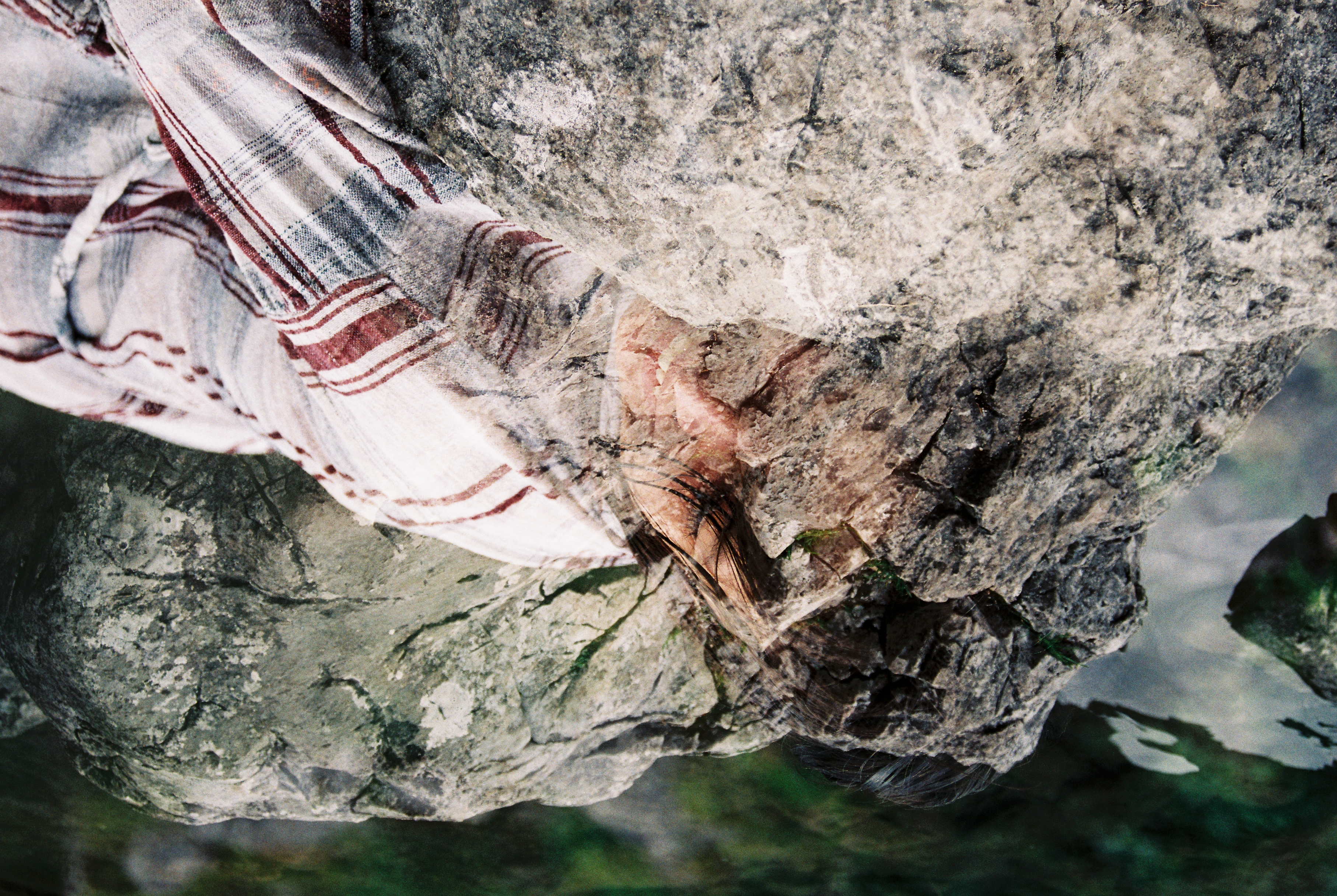 A double exposure of smiling person wearing a plaid shirt who is blending into a bed of rocks.