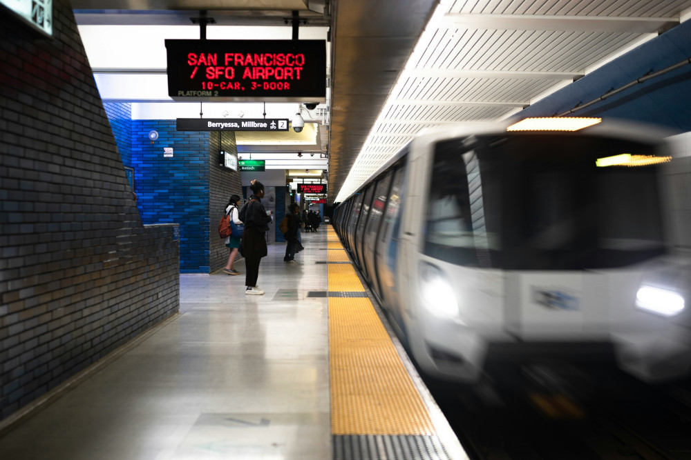 Travelers stand on a Bay Area Rapid Transit platform as a train leaves the station. (Photo by Derek Zhang / Unsplash)