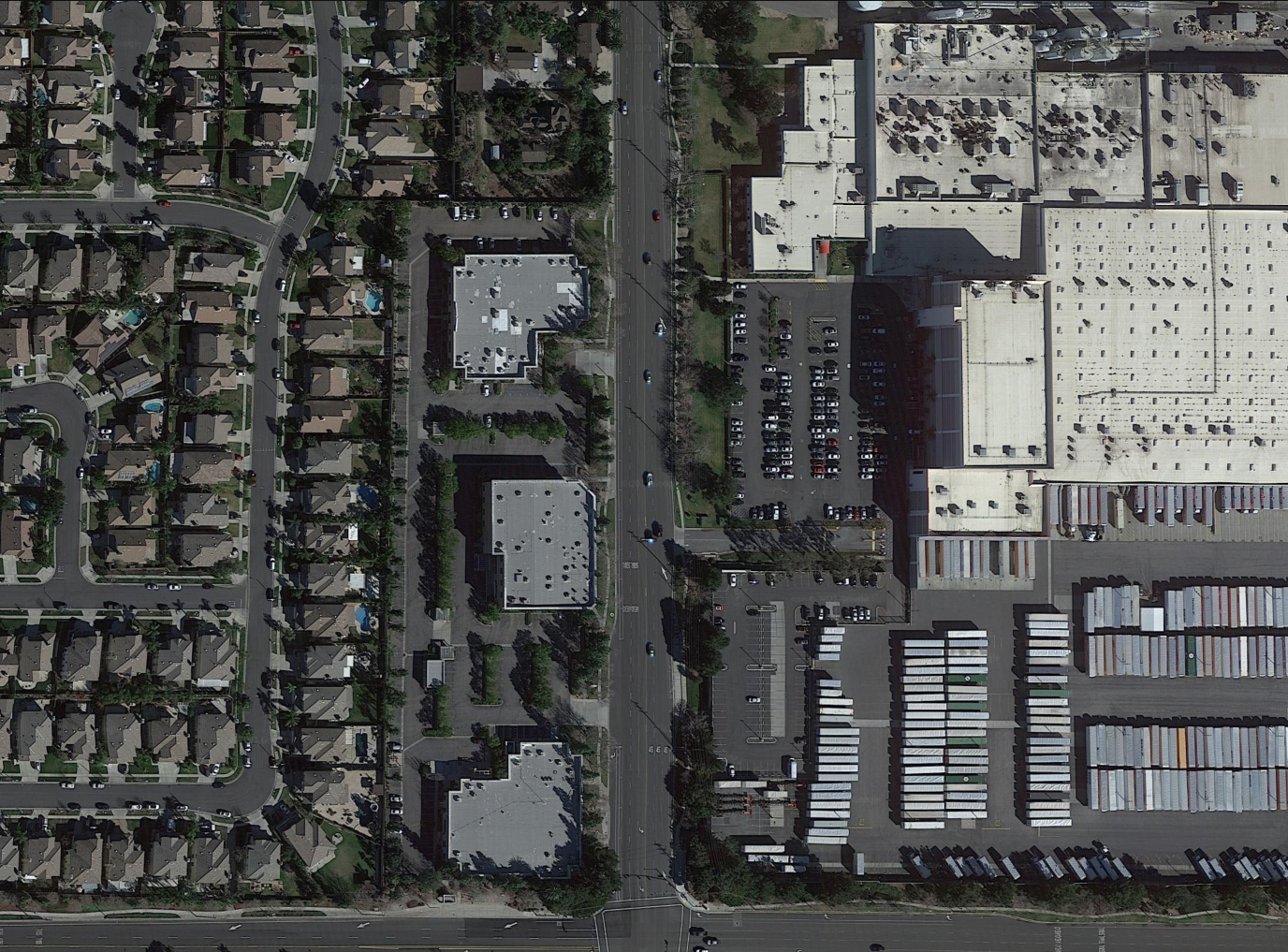 A top-down satellite's view of a warehouse and container yard. A residential neighborhood sits just across a wide street.