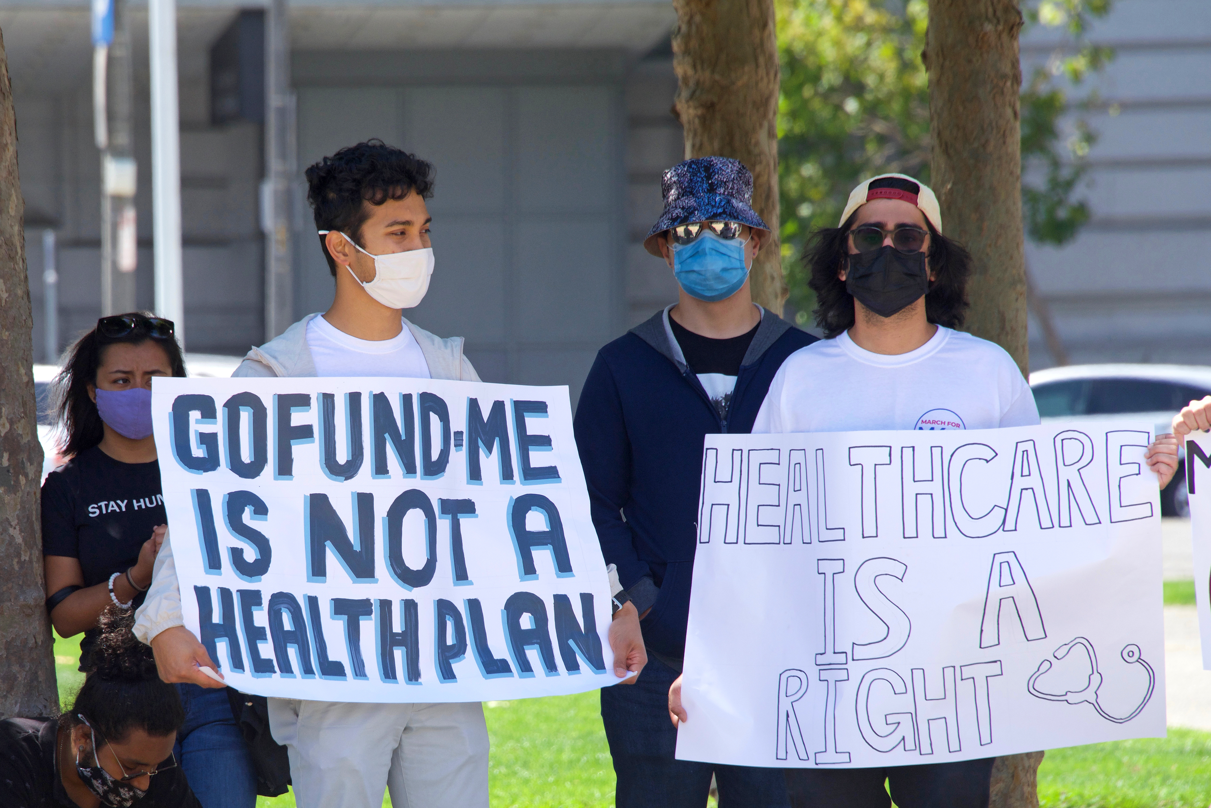 person holding sign that reads "go fund me is not a healthcare plan"