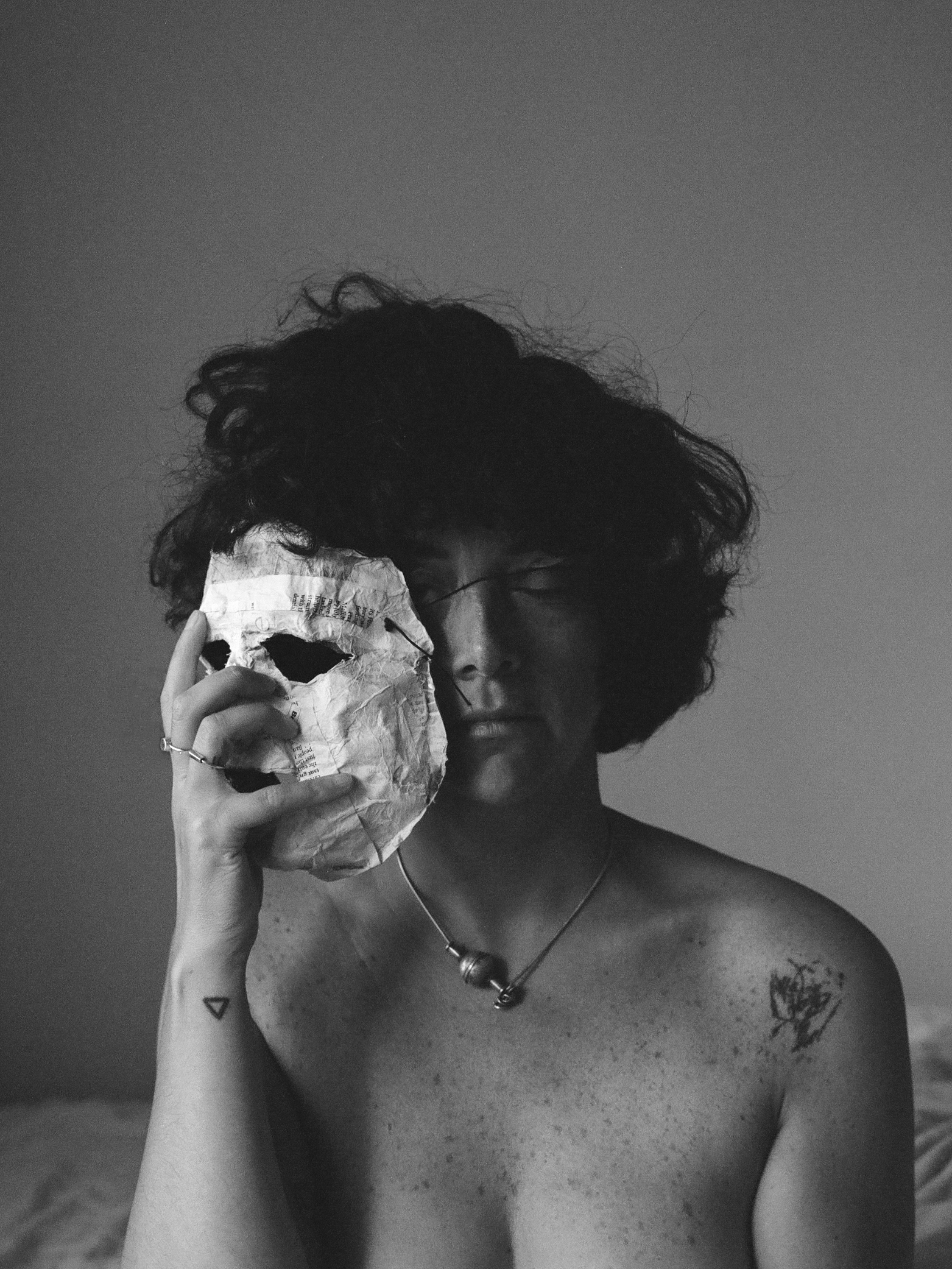 A person with short curly hair holds a papier mache mask next to their face