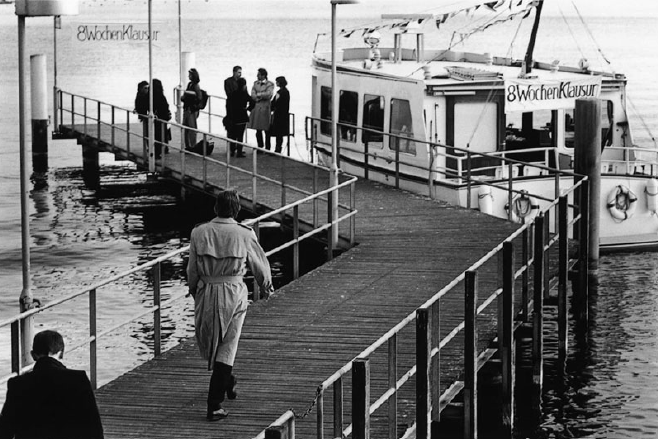 A man walking down a dock with a boat anchored nearby