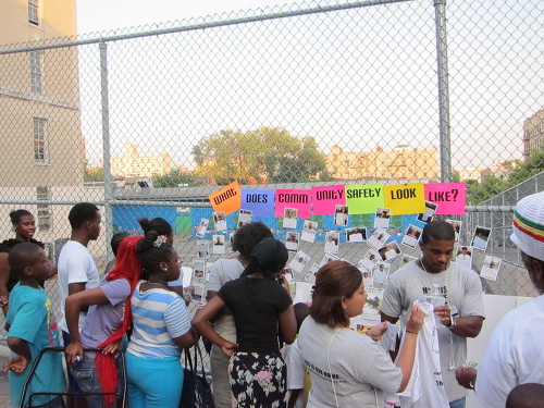 People standing in front of a fence with posters that says "what does community safety look like?"