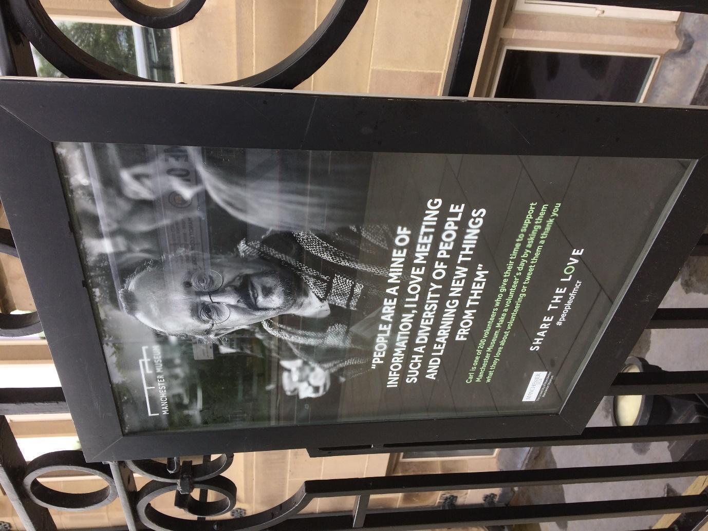 A placard featuring an older bearded man reads, "People are a mine of information, I love meeting such a diversity of people and learning new things from them."