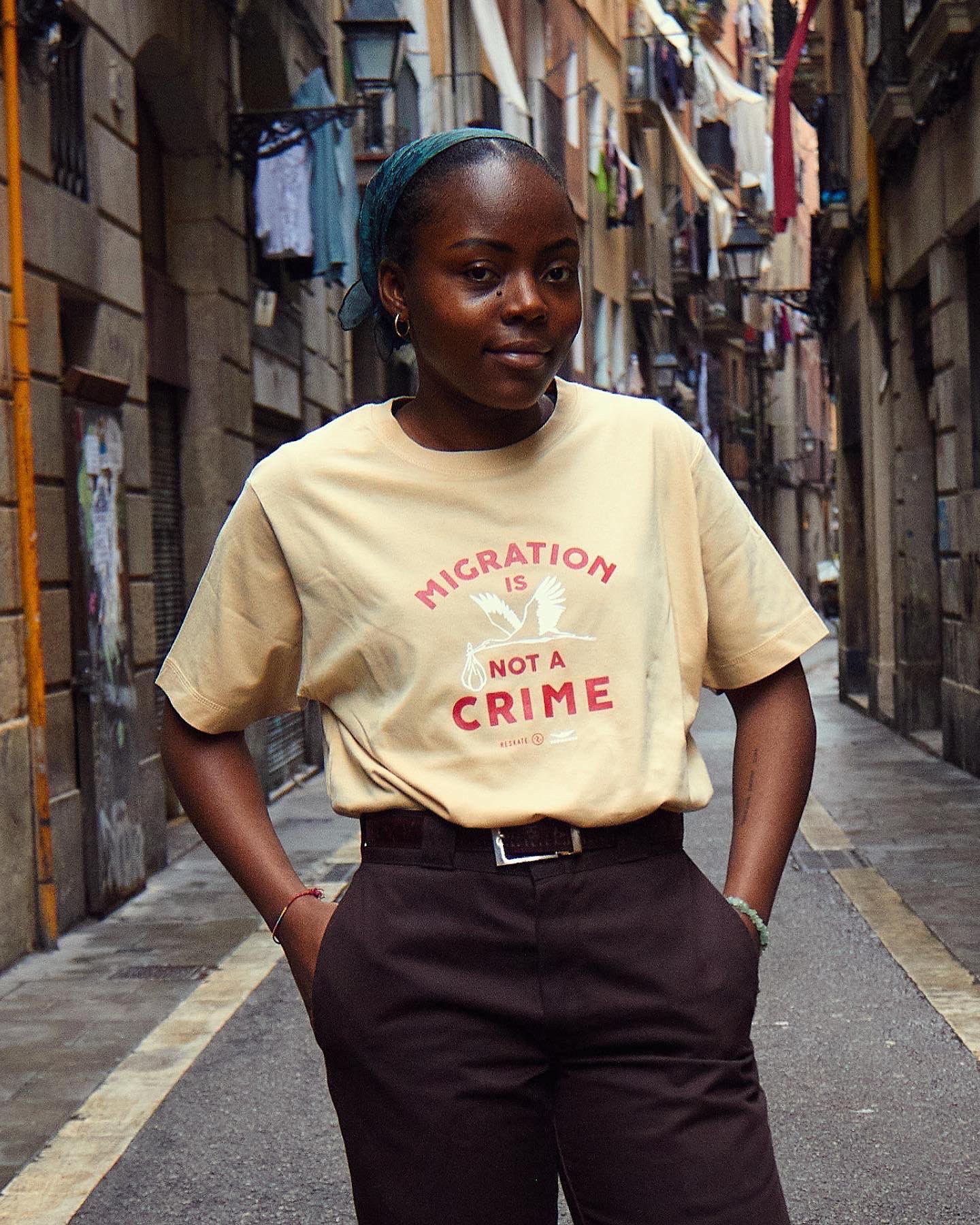 A young Black woman wears a shirt that reads "Migration is not a Crime"