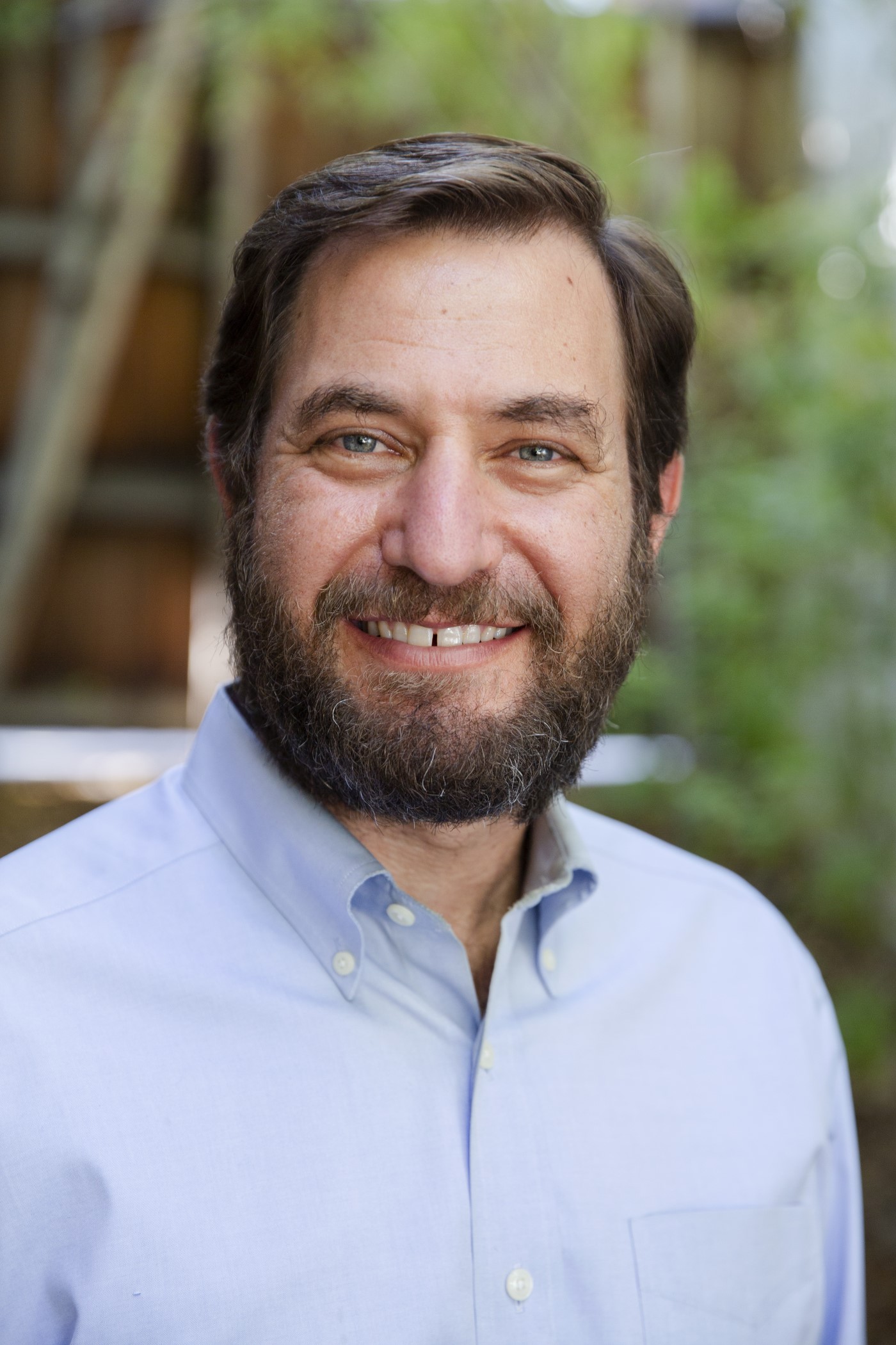 Jesse Rothstein is a bearded white man with short cropped hair and a big jovial smile that shows his teeth. He wears a big blue button up.