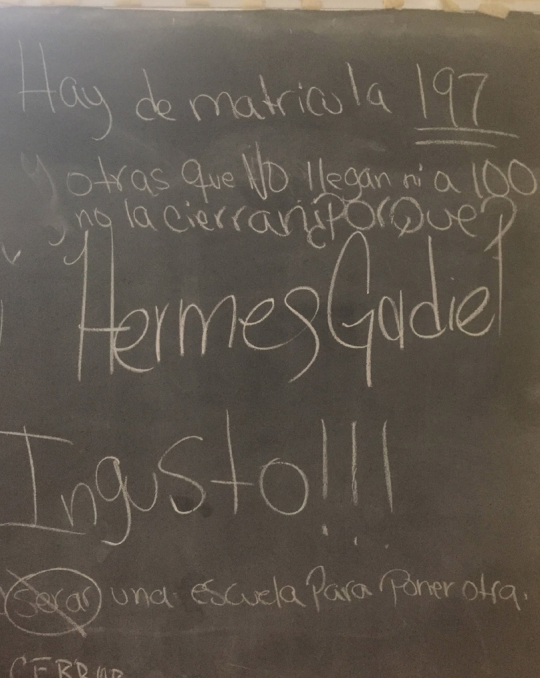 This image is of Writing on a blackboard at Pedro G. Goyco school in San Juan, questioning the reasons for closure: “There are 197 enrolled students here while schools with under 100 remain open.” Punctuation and spelling errors imply a student may have w
