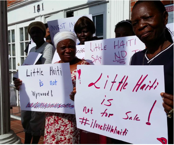 Women hold up signs that read "Little Haiti is not for sale"