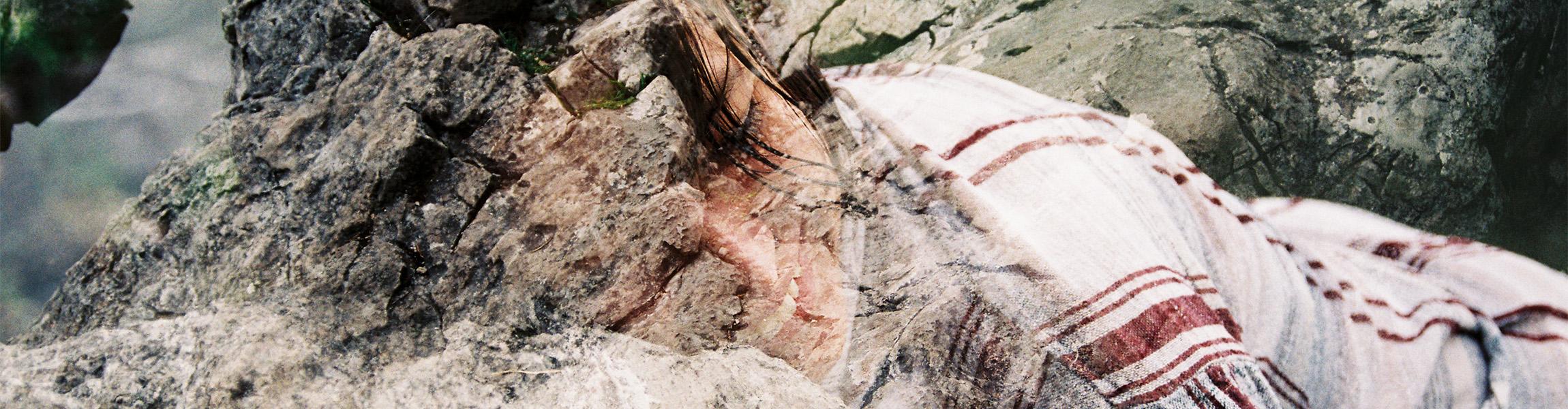 A double exposure smiling person wearing a plaid shirt who is blending into a bed of rocks.
