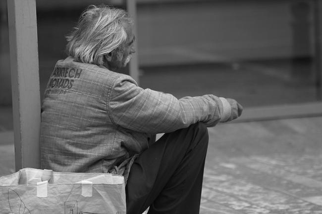 A black and white photo of a homeless man sitting on pavement