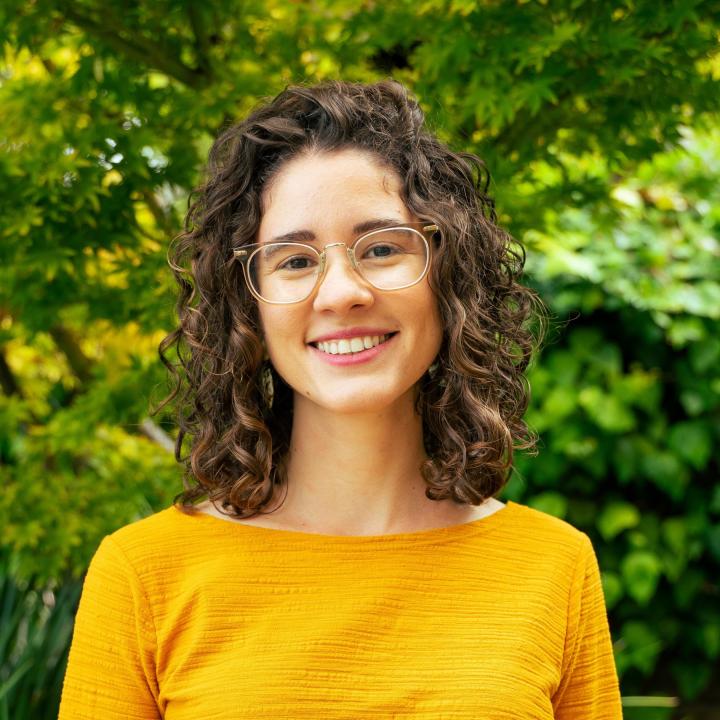 Laurent's headshot, she is a young Latinx woman with shoulder length curly brown hair, a big smile, clear-framed glasses, and a warm yellow top.
