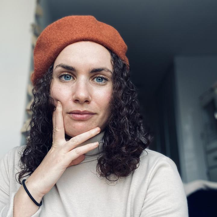 Headshot of Sara Grossman, dark hair with orange beret and tan turtleneck shirt
